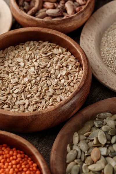 Close up view of wooden bowl with raw oatmeal near plates with pumpkin seeds, lentil and beans — Stock Photo