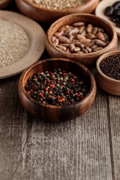 Small wooden bowls with peppercorns, seeds and beans on brown table — Stock Photo