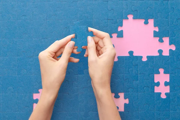 Vista recortada de la mujer sosteniendo rompecabezas azul sobre fondo rosa - foto de stock