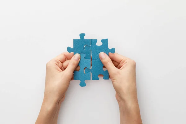 Cropped view of woman holding pieces of blue jigsaw puzzle on white background — Stock Photo