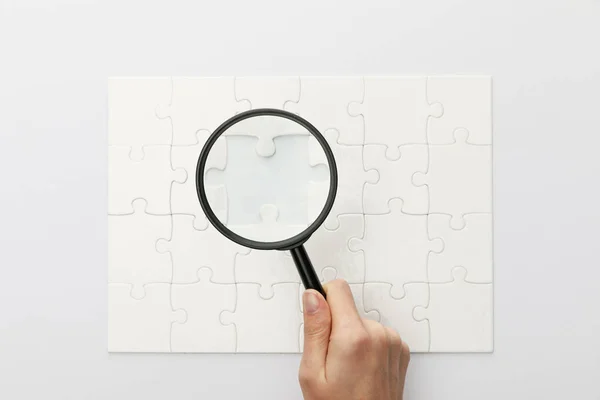 Vista ritagliata della donna che tiene lente d'ingrandimento sotto puzzle su sfondo bianco — Foto stock
