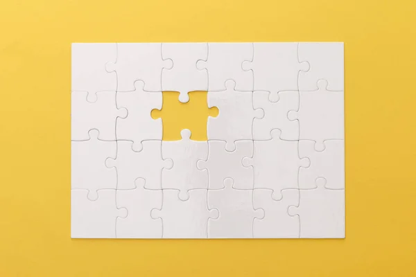 Top view of white jigsaw puzzle with lost piece on yellow background — Stock Photo