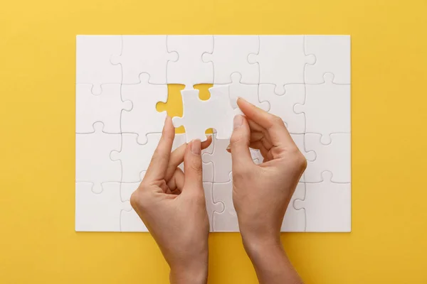 Cropped view of woman holding piece of white jigsaw puzzle on yellow background — Stock Photo