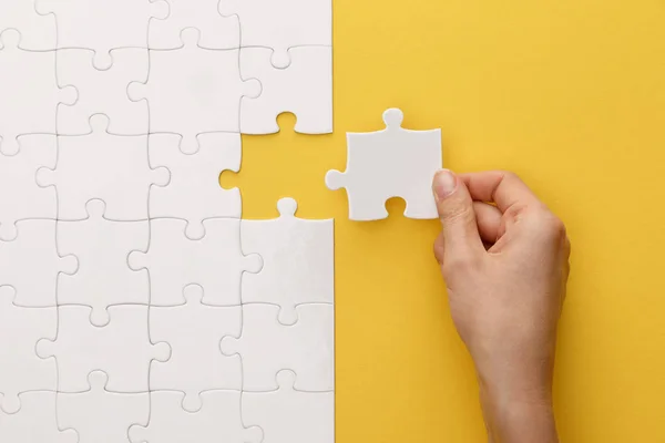 Abgeschnittene Ansicht einer Frau, die ein Stück weißes Puzzle auf gelbem Hintergrund platziert — Stockfoto