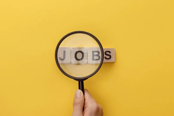 Ausgeschnittene Ansicht einer Frau mit Lupe unter Kartonquadraten mit Jobs-Schriftzug auf gelbem Hintergrund — Stockfoto