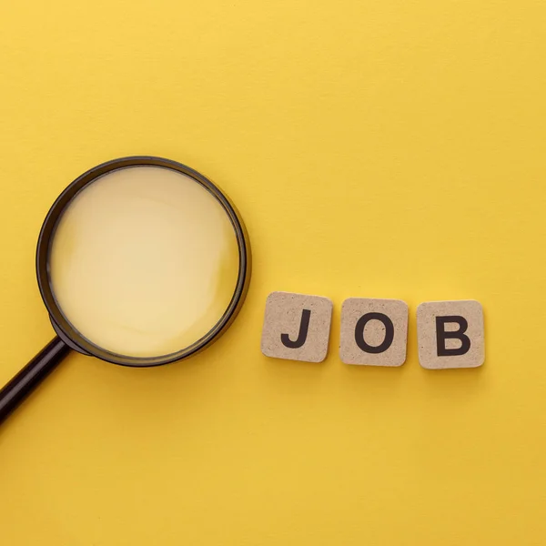 Top view of magnifying glass near cardboard squares with job lettering on yellow background — Stock Photo