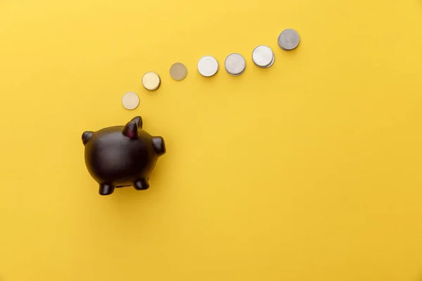 Top view of black piggy bank with coins on yellow background — Stock Photo