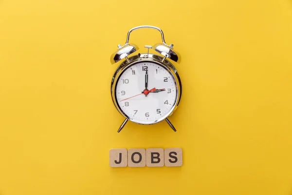 Vista dall'alto di quadratini di orologio e cartone con iscrizioni di lavori su sfondo giallo — Foto stock