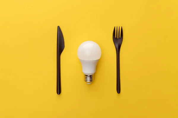 Vista superior de la bombilla entre el cuchillo y el tenedor sobre fondo amarillo — Stock Photo