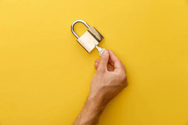 Cropped view of man holding key in padlock on yellow background — Stock Photo