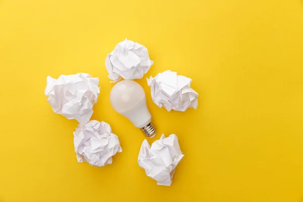 Vista superior de la bombilla entre papel arrugado sobre fondo amarillo - foto de stock