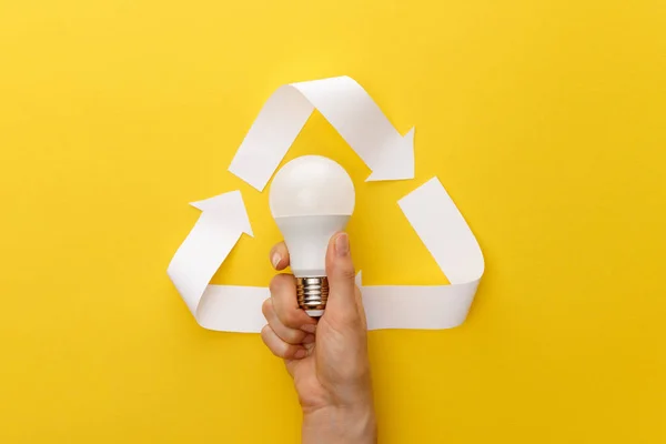 Cropped view of woman holding light bulb under paper craft triangle on yellow background — Stock Photo