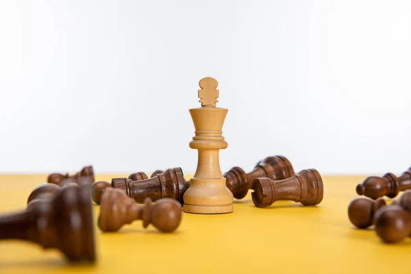 Rey de ajedrez cerca de otras figuras en la superficie amarilla aislado en blanco - foto de stock