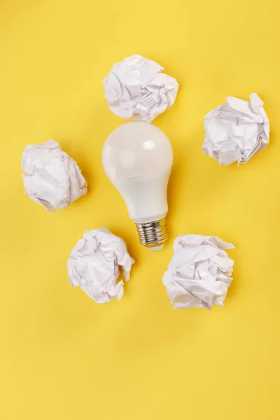 Vista superior del papel arrugado alrededor de la bombilla sobre fondo amarillo - foto de stock