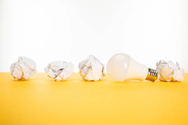 Light bulb and crumpled paper on yellow surface isolated on white — Stock Photo