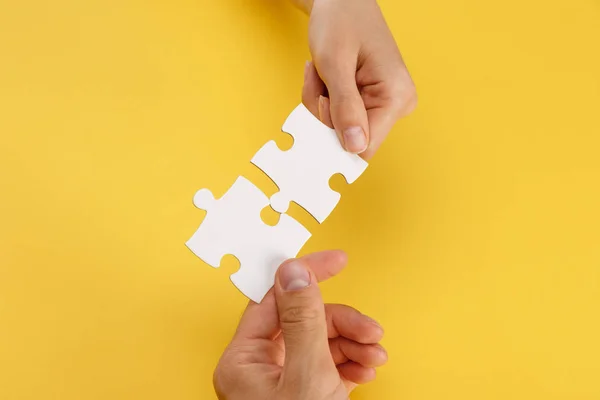 Vue recadrée de la femme et l'homme correspondant pièces de puzzle blanc sur fond jaune — Photo de stock