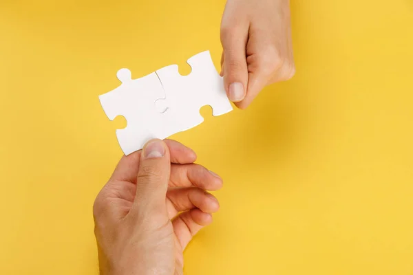 Cropped view of man and woman holding pieces of white puzzle on yellow background — Stock Photo