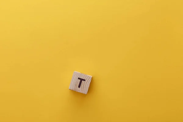 Top view of wooden cube with t letter on yellow background — Stock Photo