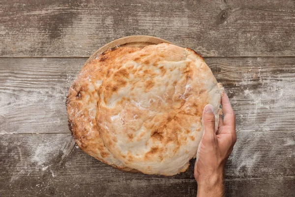 Cropped view of man holding lavash bread on wooden table — Stock Photo