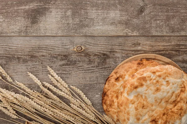 Вид сверху на хлеб лаваш рядом с шипами пшеницы на деревянном столе — стоковое фото