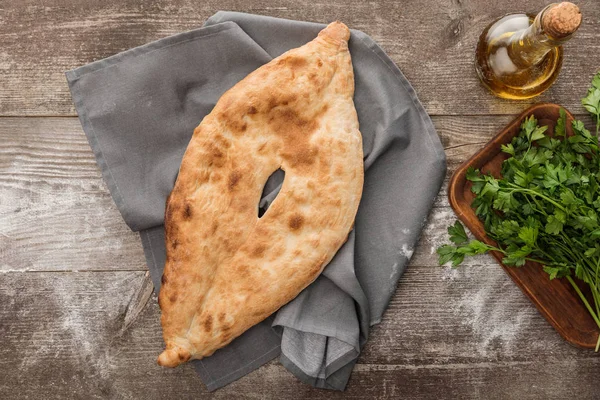 Top view of lavash bread on gray towel near fresh parsley and olive oil on wooden table — Stock Photo