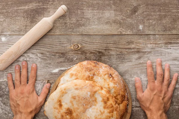 Cropped view of man near wooden table with lavash bread and rolling spin — Stock Photo