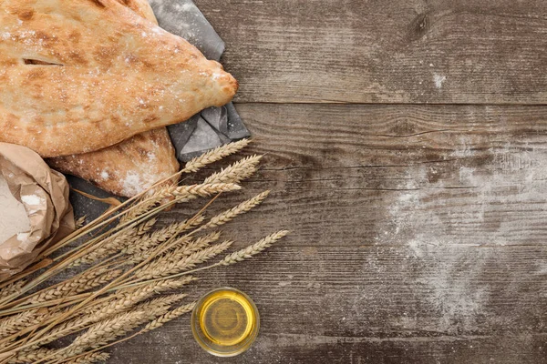 Vista dall'alto del pane lavash su asciugamano grigio vicino al pacchetto di farina, punte di grano e olio d'oliva sul tavolo di legno — Foto stock