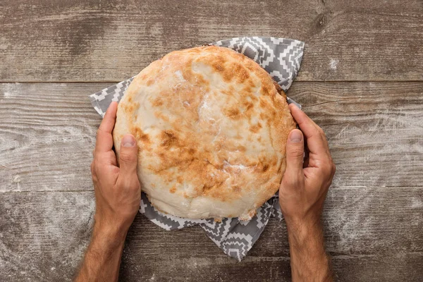 Cropped view of man holding lavash bread on gray towel with pattern on wooden table — Stock Photo