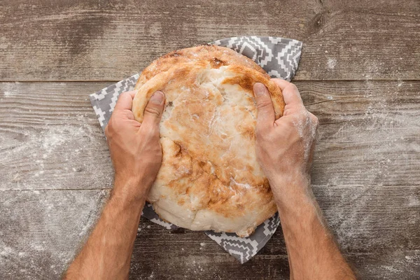 Cropped view of man splitting lavash bread on gray towel with pattern on wooden table — Stock Photo