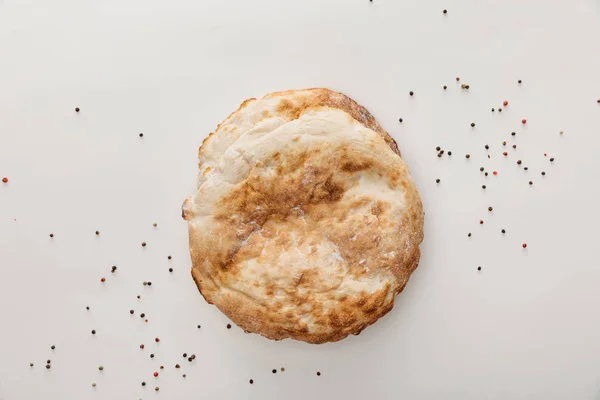 Vista superior del pan de lavash en la superficie blanca con granos de pimienta - foto de stock