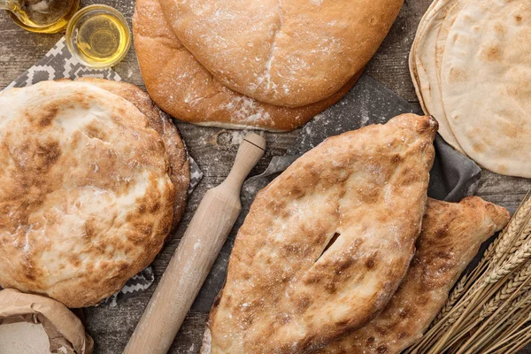 Vista dall'alto del pane lavash in diverse forme vicino al mattarello e all'olio d'oliva sul tavolo di legno — Foto stock