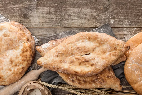 Top view of various lavash bread near rolling pin and wheat spikes on wooden table with copy space — Stock Photo