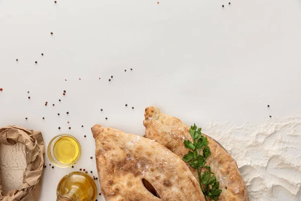Сверху вид на лаваш хлеб со свежей петрушкой рядом с мукой и оливковым маслом на белой поверхности с перцем — стоковое фото