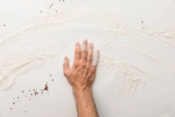 Vista recortada de la mano sobre la superficie blanca con harina y granos de pimienta - foto de stock