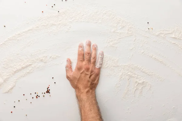 Vista ritagliata di mano su superficie bianca con farina e grani di pepe — Foto stock