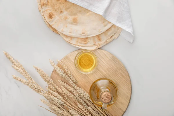 Top view of lavash bread covered with white towel near cutting board with spikes and oil on marble surface — Stock Photo