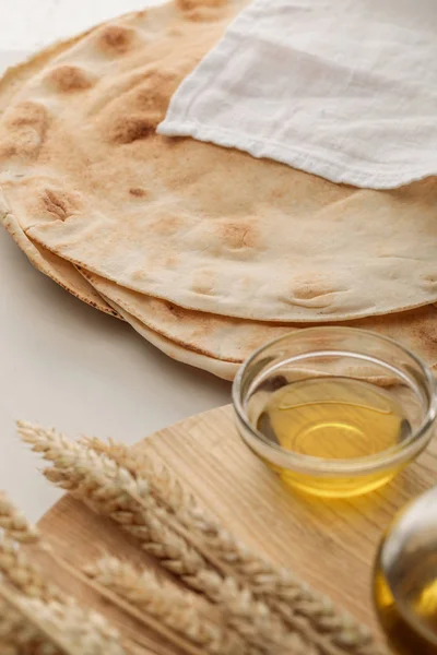 Lavash bread covered with white towel near cutting board with spikes and oil — Stock Photo