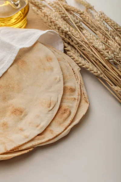 Pane lavash coperto con asciugamano vicino a punte di grano e olio su superficie bianca — Foto stock