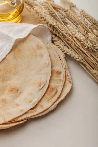 Pão lavash coberto com toalha perto de espigas de trigo e óleo na superfície branca — Fotografia de Stock