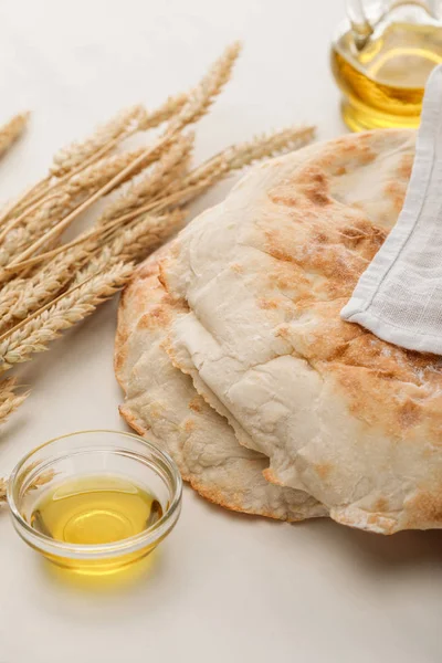 Lavash bread covered with towel near spikes and oil on white surface — Stock Photo