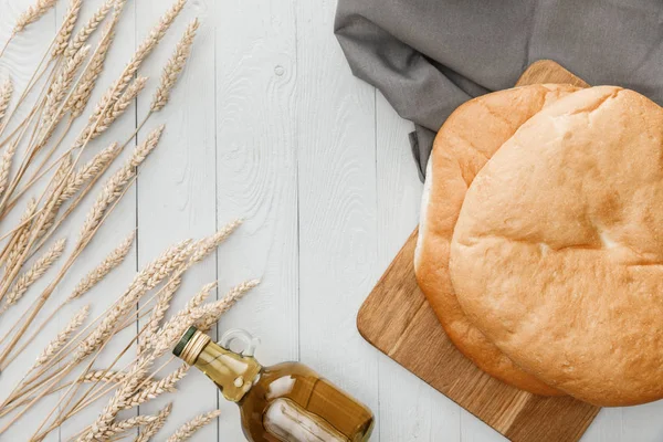 Vista superior del pan de lavash en la toalla cerca de espigas y aceite de oliva en la superficie de madera blanca - foto de stock