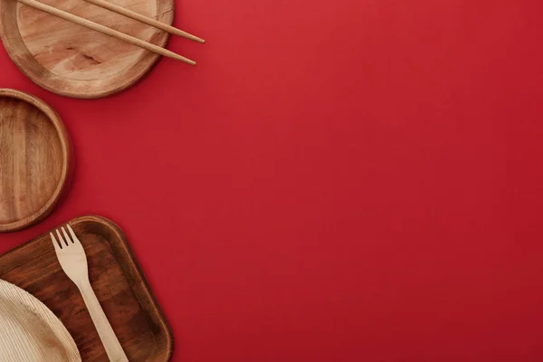 Vue de dessus des plats en bois avec fourchette et baguettes sur fond rouge — Photo de stock