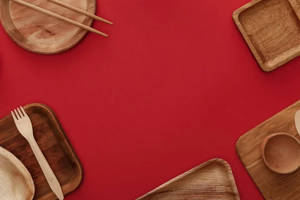 Vista superior de platos de madera, taza, tenedor y palillos sobre fondo rojo - foto de stock