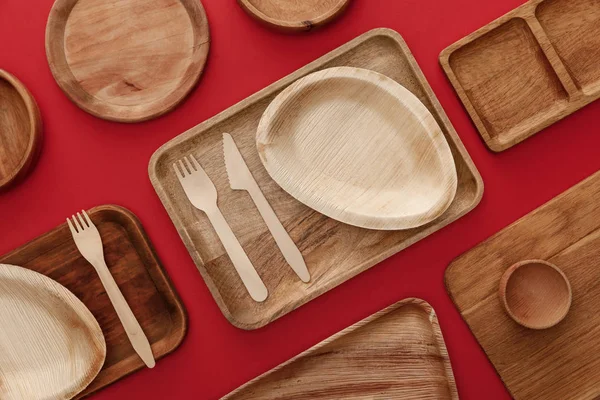 Vista superior de platos de madera ecológicos, platos y cubiertos sobre fondo rojo - foto de stock