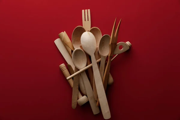 Vista superior de cucharas de madera ecológicas, tenedor y utensilios de cocina sobre fondo rojo — Stock Photo