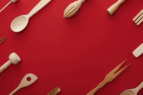 Vue de dessus des cuillères en bois naturel, fourchette et ustensiles de cuisine sur fond rouge avec espace de copie — Photo de stock