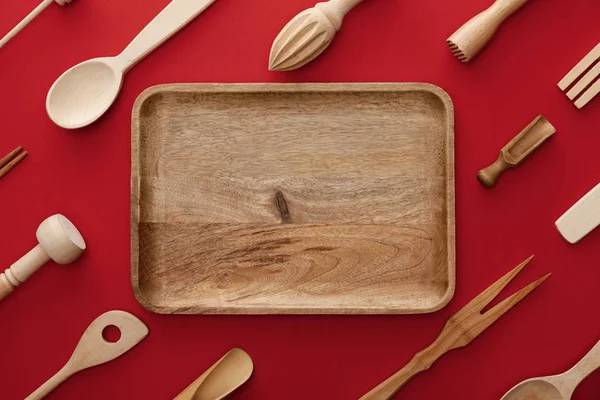 Draufsicht auf natürliche rechteckige Holzschale auf rotem Hintergrund mit Geschirr — Stockfoto