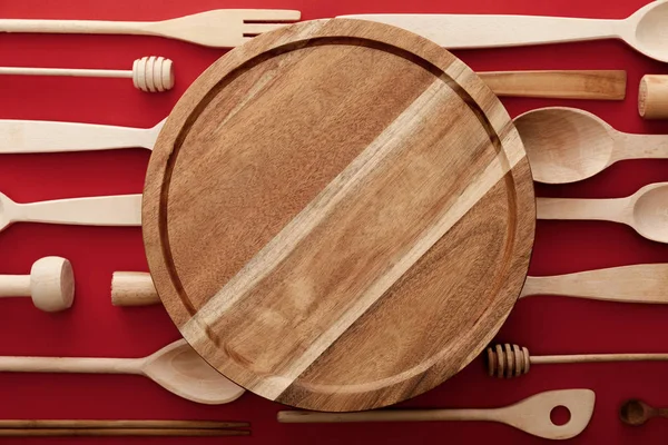 Top view of round wooden cutting board on red background with kitchenware — Stock Photo