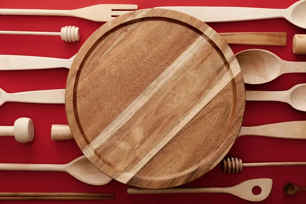 Vista superior de tabla de cortar de madera redonda sobre fondo rojo con utensilios de cocina — Stock Photo