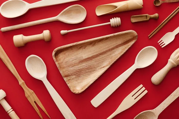 Vista superior do prato de madeira triângulo vazio no fundo vermelho com utensílios de cozinha — Fotografia de Stock